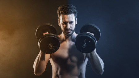 Attractive shirtless man exercising and lifting weights on dark background, strength conceptの写真素材
