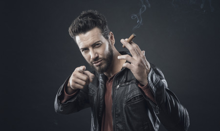 Confident fashionable man in leather jacket smoking a cigarの写真素材