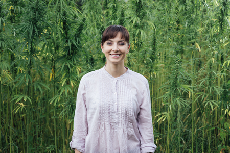 Smiling woman wearing a white new age shirt and posing in a hemp fieldの写真素材