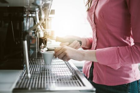 Young waitress making coffee with an espresso coffee machine, she is holding a cup and the filter holderの写真素材