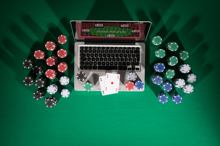 Poker and casino online gaming concept with laptop, cards and stacks of chips on green table, top...