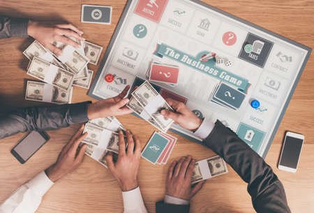 People playing a business board game on a wooden table, one player is paying with dollar packs hands close up, top viewの写真素材