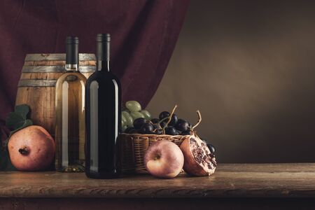 Wine bottles, barrel and fruit basket on a rustic wooden table, red drape on background, still lifeの写真素材