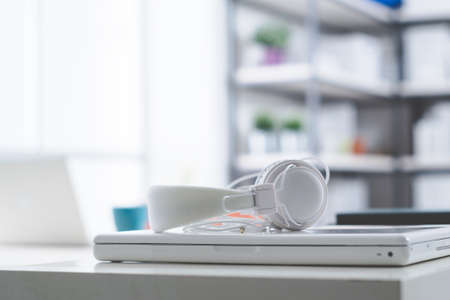 White laptop and headphones on a table, shelves and window in the background, teenager room conceptの写真素材