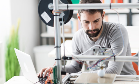 Young designer engineer using a 3D printer in the laboratory and studying a product prototype,...