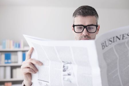 Confident businessman with glasses reading a financial newspaper in his office