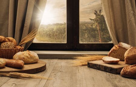 Freshly baked bread on a chopping board on the kitchen table in front of a window, healthy eating conceptの写真素材