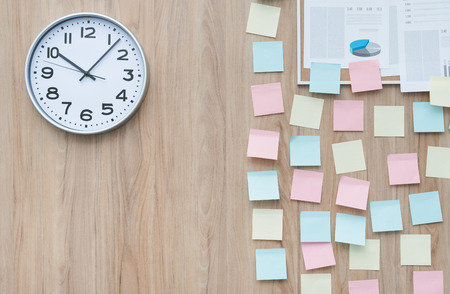Office wall partially covered with colorful stick memo notes and a clock, ideas and deadlines conceptの写真素材