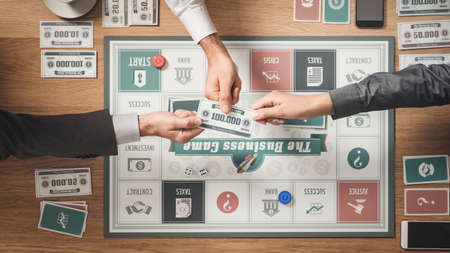 People playing a business board game on a wooden table challenging each other and holding a banknoteの写真素材