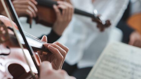 Violinist performing on stage with classical music symphony orchestra, hands close up, selective focus, unrecognizable peopleの写真素材