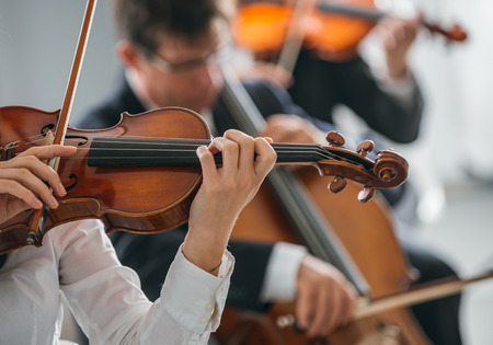 Female violinist performing and classical orchestra on background, selective focus, music and arts conceptの写真素材