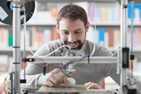 Young designer engineer using a 3D printer in the laboratory and studying a product prototype,...