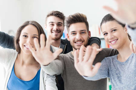 Cheerful group of friends posing and greeting with hands up, friendship and enjoyment concept