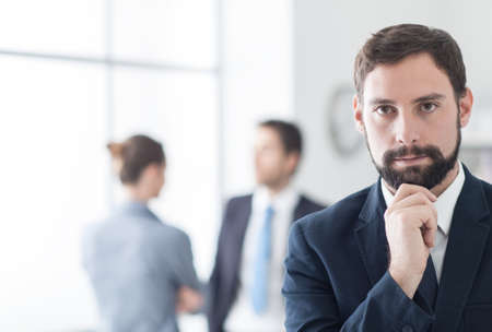 Successful young businessman posing in his office, business team in the backgroundの写真素材
