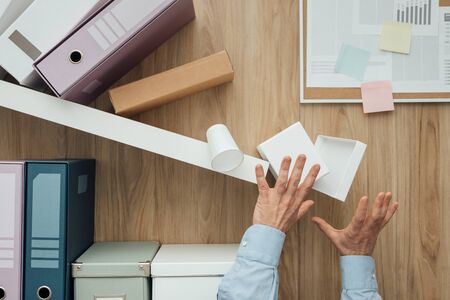 Shelf crashing and folders falling down on a office worker, failure and disaster conceptの写真素材
