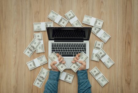 Man with a load of cash money using a laptop: winning, earning and earning conceptの写真素材