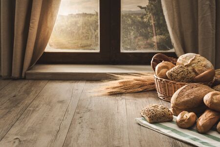 Fresh bread on the kitchen table in front of a window with a countryside panorama, healthy eating and traditional bakery conceptの写真素材