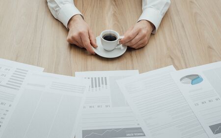 Manager working at office desk, he is viewing a financial report with charts and drinking a coffeeの写真素材