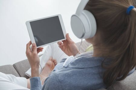 Woman sitting on the couch at home in the living room, she is connecting with a digital tablet and...