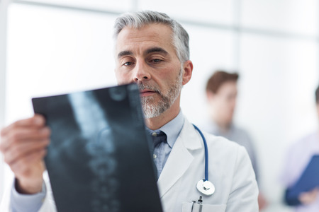 Radiologist examining a patient's x-ray, medical staff on the background, healthcare conceptの写真素材
