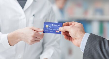 Man at the pharmacy making purchases with a credit card, he is giving the card to the female pharmacist, hands close upの写真素材