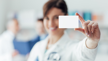 Smiling female doctor holding a blank business card, selective focus, business and healthcare conceptの写真素材