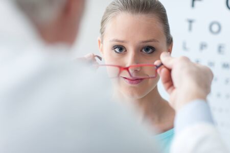 Optician giving new glasses to the patient, she is smiling and looking at camera, eye care concept