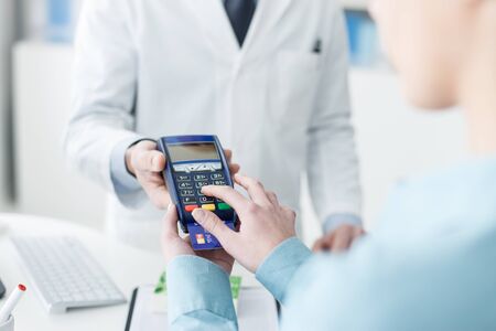 Woman shopping at the pharmacy with a credit card and entering a security pin on the terminal, hands close upの写真素材