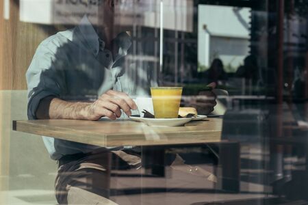 Man having breakfast at the cafe next to a window with reflectionsの写真素材