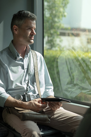 Man traveling by bus and using a digital tablet, he is working and looking through a window