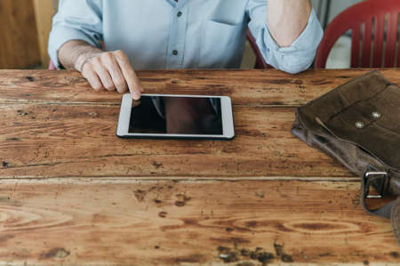 Confident smiling man using a digital tablet on a rustic wooden table, hands close upの写真素材