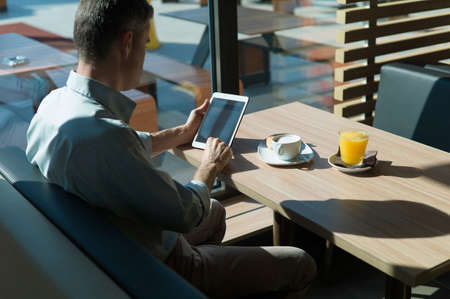 Businessman having an healthy relaxing breakfast at the bar, he is using a digital touch screen...