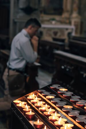 Religious man kneeling at the pew in the Church and praying with hands claspedの写真素材