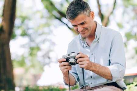 Smiling photographer at the park, he is sitting and watching picture previews on the camera displayの写真素材