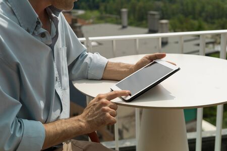 Man relaxing at the terrace bar in the wi-fi area, he is using a digital touch screen tablet and connecting to the webの写真素材