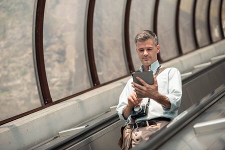 Tourist on the escalator, he is connecting with a touch screen tablet and searching for directionsの写真素材