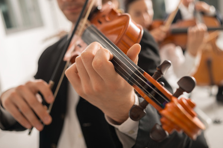 Violinist performing on stage with classical music symphony orchestra, hands close up, selective focus, unrecognizable peopleの写真素材