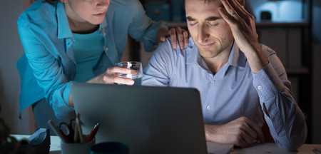 Wife comforting her depressed husband and giving him a glass of water, he is having an headache and feeling sickの写真素材