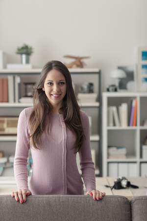 Confident young woman at home posing in the living room, she is smiling at cameraの写真素材