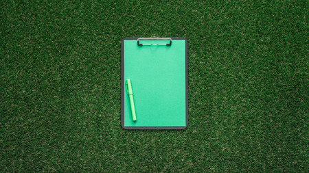 Green sheet and clipboard on lush grass, creativity and ecology concept
