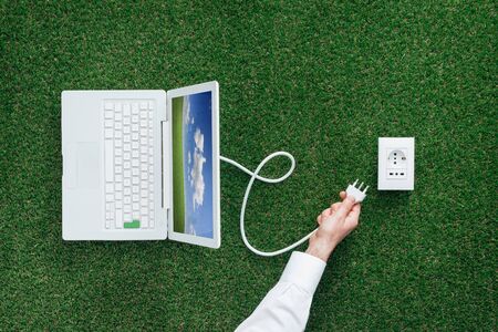 Man plugging a laptop into a socket on the grass, green renewable energy and power generation conceptの写真素材
