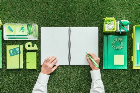 Businessman writing on a notebook on a grass desktop; environmental care, business and planning...