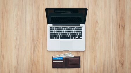 Laptop and wallet with credit card and cash money on a wooden desktop, online payment systems and banking conceptの写真素材