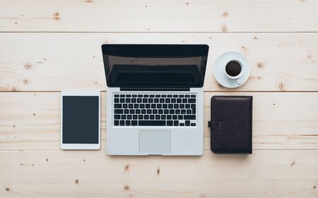 Minimal office workspace: laptop, tablet, organizer and coffee on a wooden desktop, flat lay