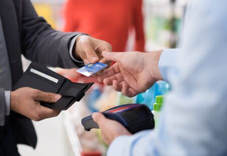 Man doing grocery shopping at the supermarket and paying with a credit card at the store checkoutの写真素材