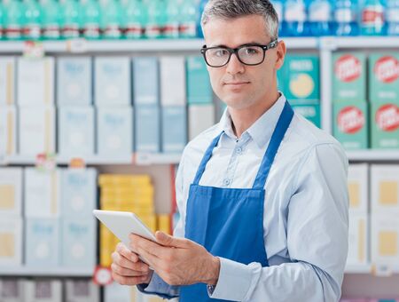 Professional supermarket clerk using a touch screen tablet and working, he is smiling at cameraの写真素材