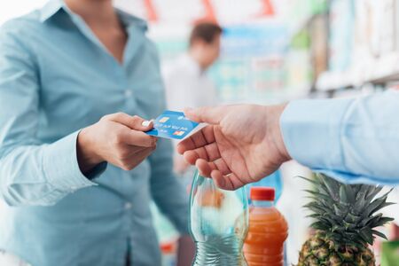 Woman at the supermarket checkout, she is giving her credit card to the cashier, retail and payments conceptの写真素材