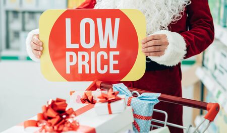 Santa Claus doing grocery shopping at the supermarket and holding a discount sign, Christmas and...