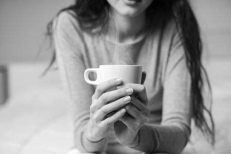Young woman sitting on the bed at home and having a cup of coffee, lifestyle and relax conceptの写真素材
