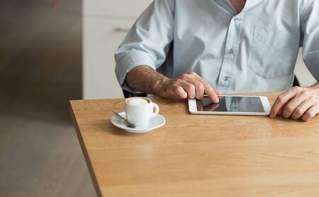 Man having a relaxing coffee break at home and using a digital tablet, hands close up